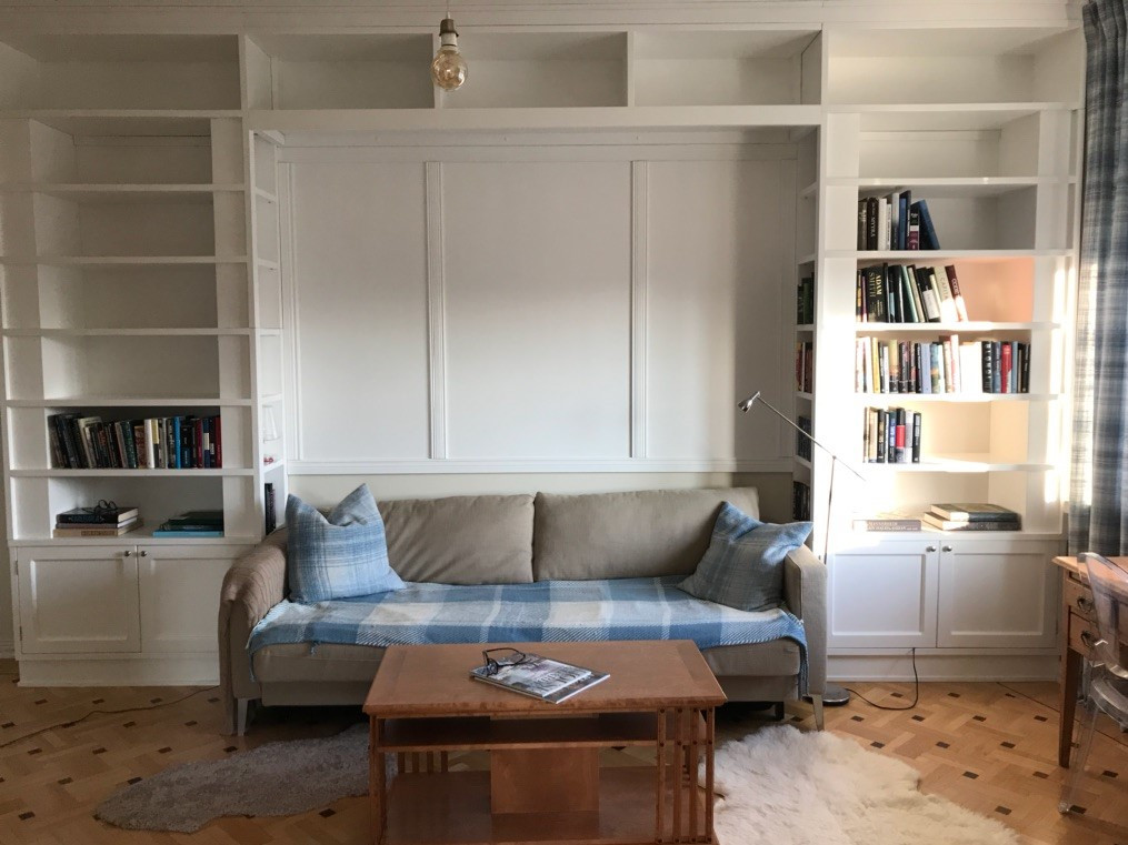 Build-in kirjahylly männystä, valkoiseksi maalattuna. Keskellä sohvatila. Ylhäällä hyllytilaa.