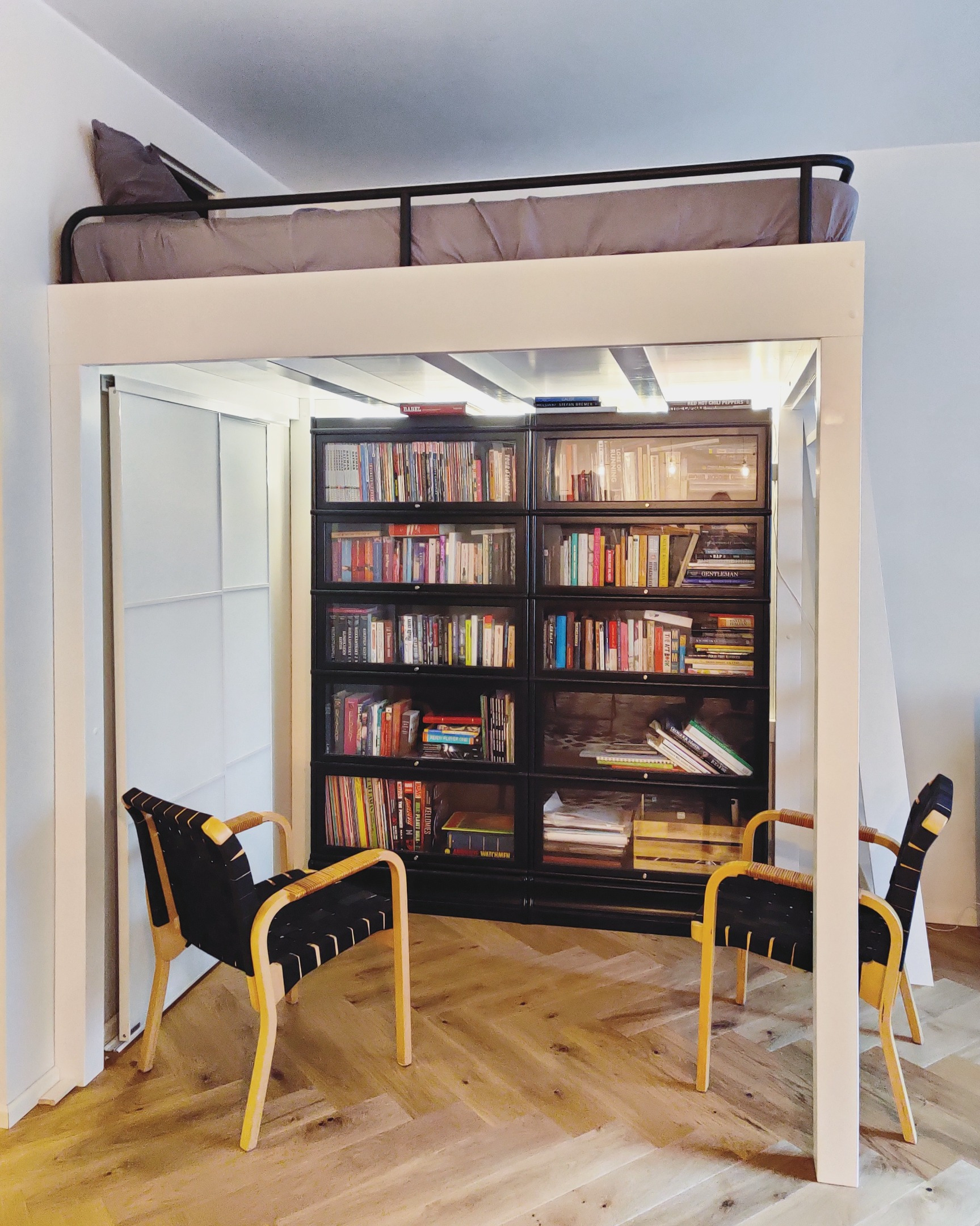 Korotettu sänky vaatetangollisilla vetolaatikoilla ja kirjahyllyllä