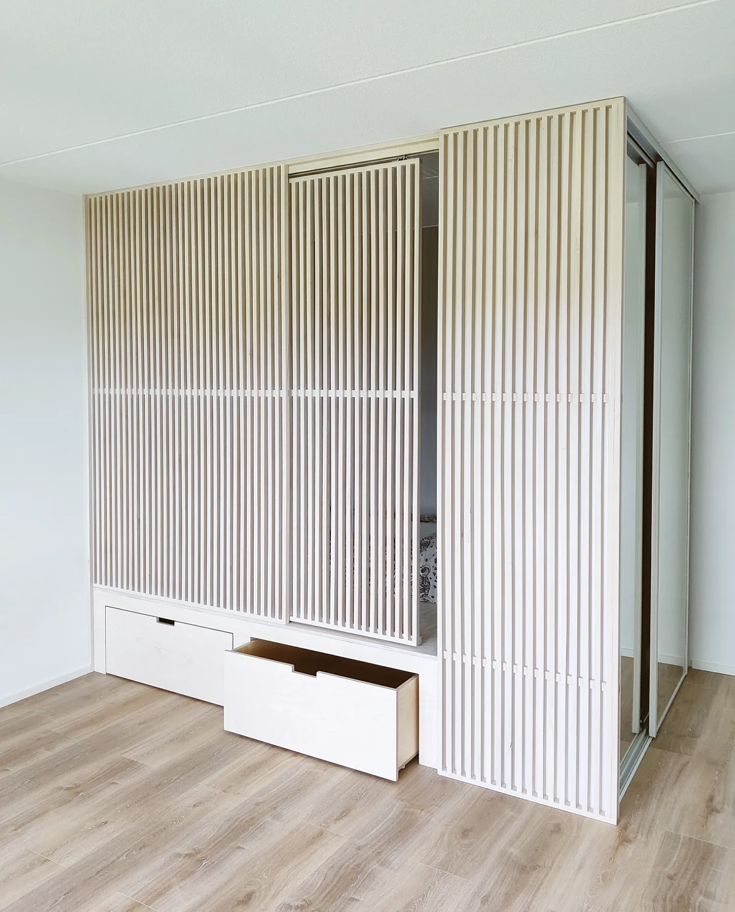 Korotettu sänky, jonka päädyssä vaatekaapit. Edessä liukuovellinen rimaseinä, alla kaksi isoa pyörällistä vetolaatikkoa