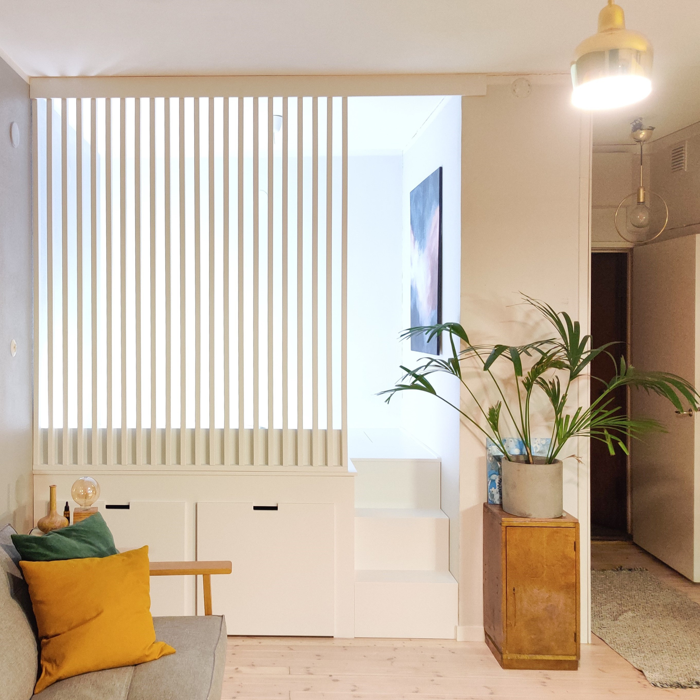 Alkovin korotettu sänky vetolaatikoilla ja rimaseinällä, jossa portaat on upotettu alkovin sisään.