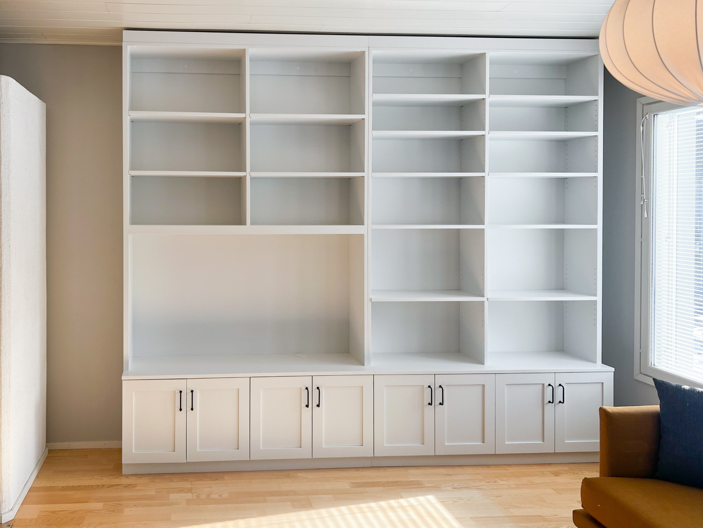 Kirjahylly koivusta maalattuna. Alhaalla kehysovelliset kaapit, yläpuolella tila tv:lle ja korkeussäädettävät hyllylevyt.