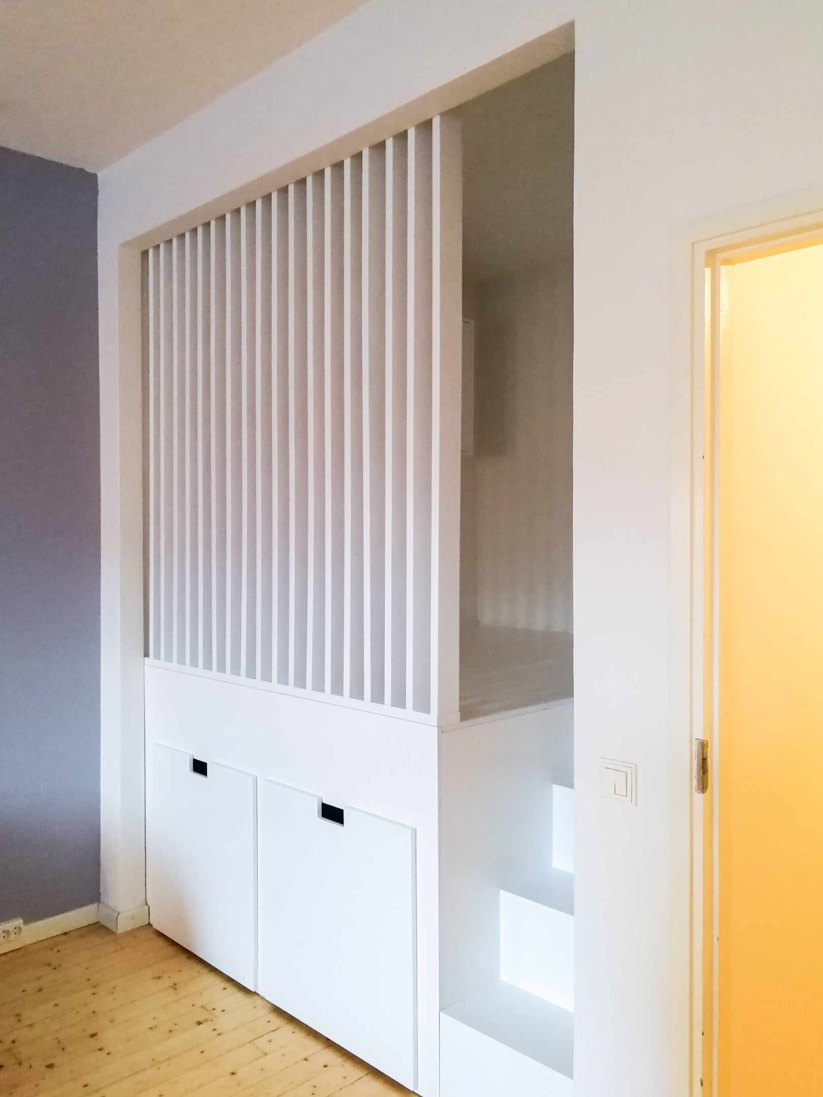 Alkovin korotettu sänky vetolaatikoilla ja rimaseinällä. Portaat upotettuna alkovin sisään. 