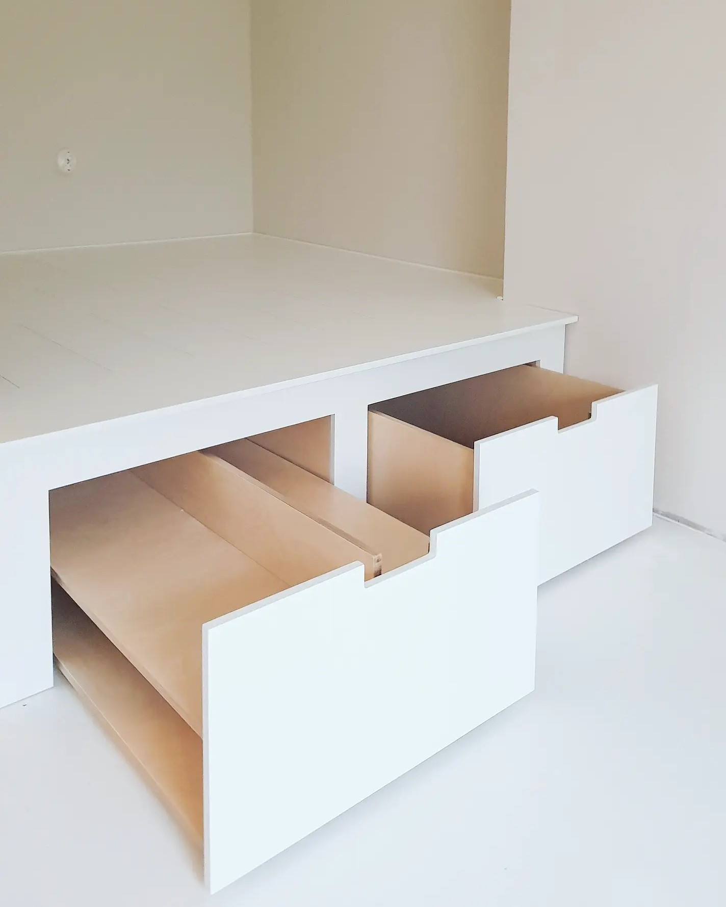 Alkovin korotettu sänky pyörällisillä laatikoilla. Toisessa laatikossa jaot kenkien säilytystä varten.