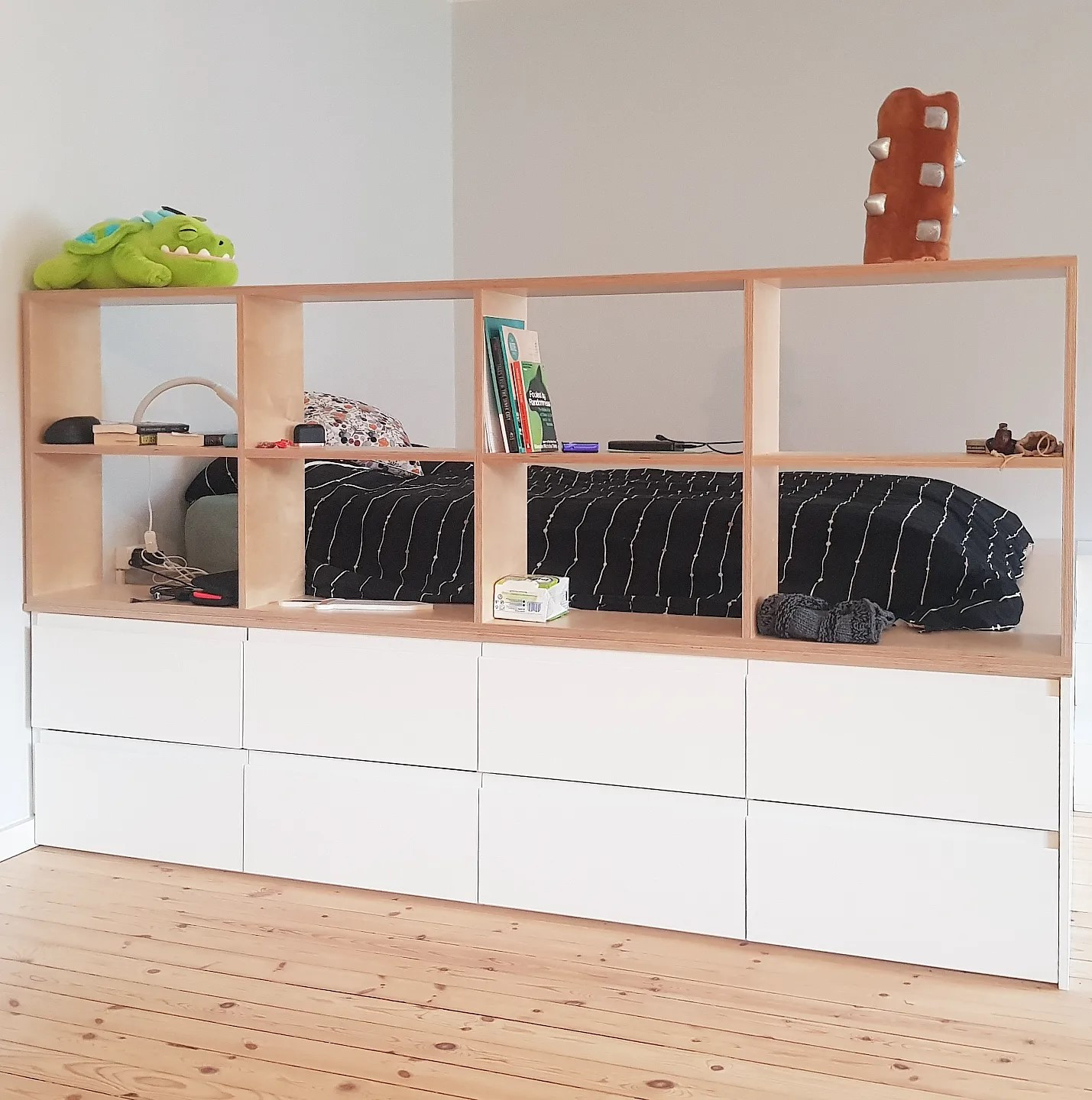 Korotettu sänky, jonka alla vaatteiden säilytystä varten kahdeksan kiskollista vetolaatikkoa. Patja uppoaa osittain pohjaan. Päällä kirjahylly tilanjakajana.